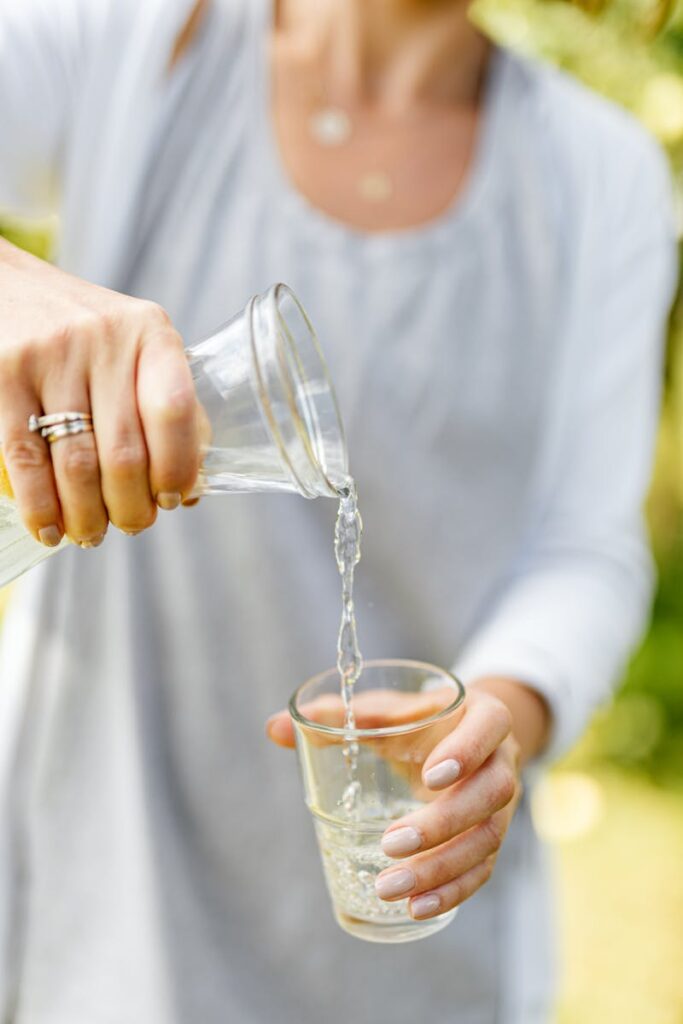 Woman with rings pours water into a clear glass, showcasing hydration and lifestyle.